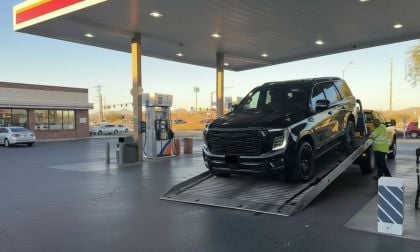 Black 2025 GMC Yukon being loaded onto a flatbed tow truck at a gas station during sunset.