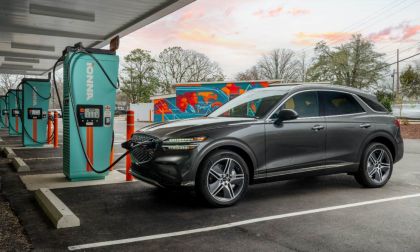 Dark gray Genesis GV70 SUV parked at Ionna charging station during sunset with vibrant pink and orange sky