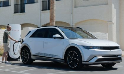 White 2025 Hyundai Ioniq 5 charging at a Tesla Supercharger station in a parking lot.