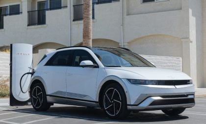 White Hyundai IONIQ 5 electric SUV charging at Tesla station, sleek modern design with black wheels