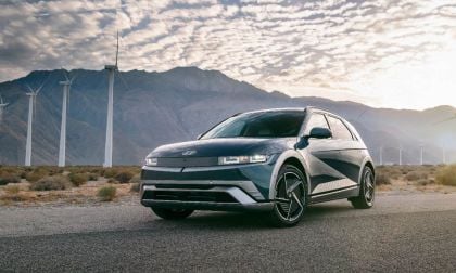Dark green Hyundai Ioniq 5 electric SUV parked on desert road with wind turbines and mountains in background at sunrise