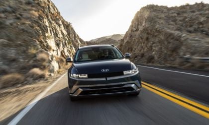 Blue Hyundai SUV driving on mountain road between tall rocky cliffs at sunset