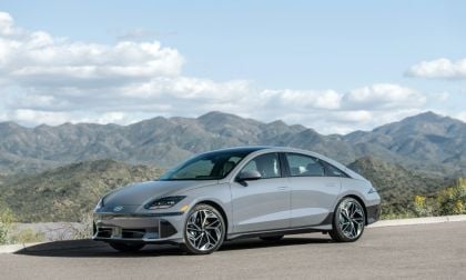 Silver sedan parked on a road with mountains and cloudy sky in the background.