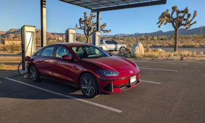 Red 2025 Hyundai Ioniq 6 electric sedan parked at charging station in Joshua Tree desert, mountains visible, three-quarter front view.