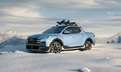 Light blue pickup truck with roof rack on snowy terrain, mountains in the background.