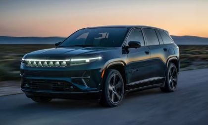 2025 Jeep Wagoneer in deep blue, driving on highway at sunset with mountain silhouette, LED headlights glowing