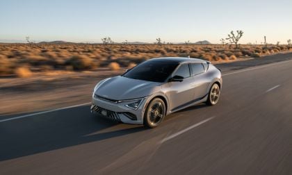 2024 Kia EV6 GT in metallic silver, photographed at three-quarter front angle driving through desert landscape with Joshua trees at sunset.