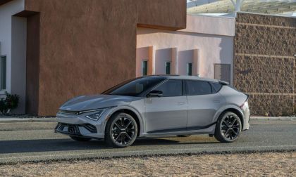 Silver electric car parked on a street beside a modern building with textured walls.