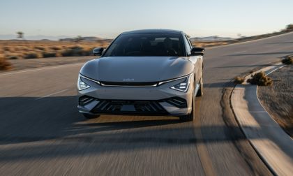 Silver Kia EV6 driving on winding desert road at sunset, front view