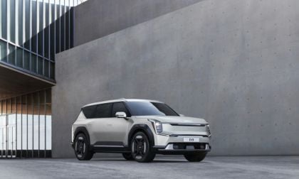 2025 Kia EV9 silver exterior shown from front three-quarter angle in a modern architectural setting, emphasizing large wheels and rugged electric SUV stance.