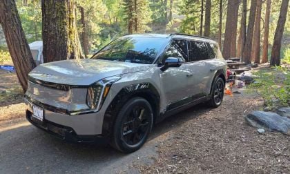 A silver SUV parked at a forest campsite with trees and a picnic table nearby.