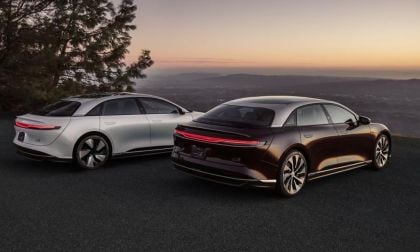 Two sleek, modern electric cars in white and dark tones parked against a scenic sunset backdrop, showcasing elegant design features.