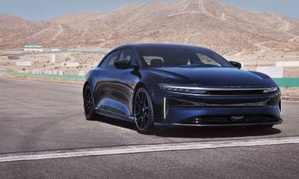 A sleek black Lucid Air luxury electric vehicle parked on a racetrack, with desert mountains in the background under a clear blue sky.
