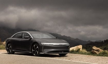 Black Lucid Air sedan parked on mountain road with dramatic cloudy sky and rocky landscape backdrop