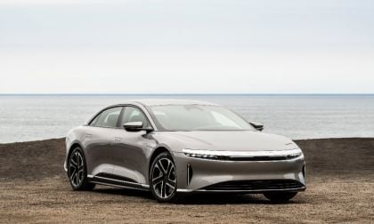 Silver 2025 Lucid Air electric sedan parked on rocky terrain with calm ocean horizon in background, sleek aerodynamic profile and distinctive LED headlights