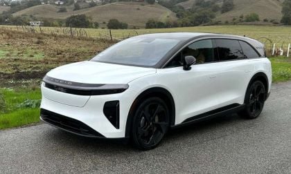 2025 Lucid Gravity electric SUV in pearl white, shown at three-quarter front angle on rural mountain road, featuring sleek aerodynamic design and black contrast elements.