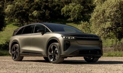 Lucid Gravity electric SUV in metallic gray, parked on dirt with lush green forest background