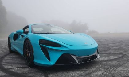 A turquoise 2025 McLaren Artura parked on a misty road, showcasing sleek lines and bold black wheels.