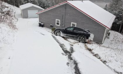 Black Ford Mustang Mach-E parked on a snowy driveway beside a house, showing winter driving conditions and snow-covered landscape.