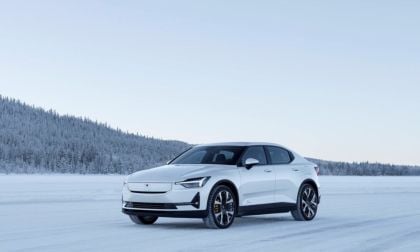 A sleek white electric car parked on a snow-covered landscape, surrounded by snow-laden trees under a clear sky.