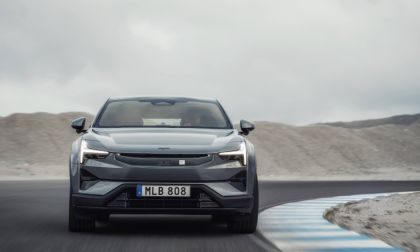 Silver car driving on a curved road with a mountainous background under cloudy skies.