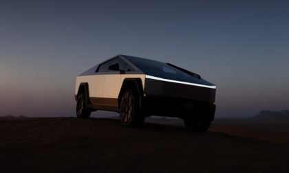 Tesla Cybertruck parked on desert ground at dusk, angular stainless steel body gleaming against dark gradient sky