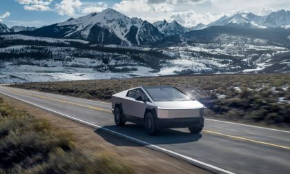 Tesla Cybertruck driving on mountain road with snow-capped peaks and valley in background