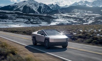Tesla Cybertruck driving on mountain highway with snow-capped peaks and winter landscape backdrop