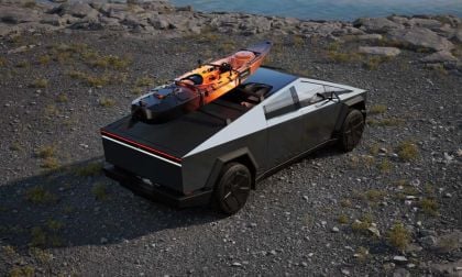 A black and silver futuristic vehicle parked on rocky terrain, with a kayak secured on top, beside a tranquil water scene.