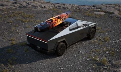 A futuristic black and silver electric truck parked on rocky terrain, with an orange kayak secured on its roof.