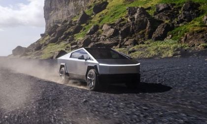 A futuristic looking silver Tesla cybertruck speeds along a rugged, rocky path with green moss and towering cliffs, emitting dust and conveying a sense of power and adventure.