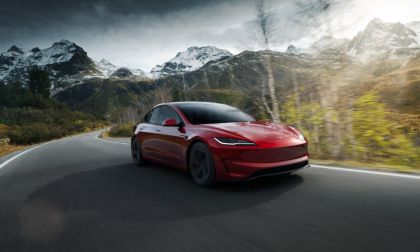 Red Tesla Model S driving on mountain road with snow-capped peaks in background