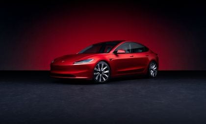 Candy red Tesla Model 3 sedan shown in three-quarter front view against dark background, featuring sleek aerodynamic design and signature LED headlights.