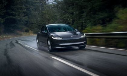 Black Tesla Model 3 navigating a wet, curved forest road with blurred motion and dynamic driving stance