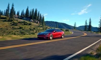 Red car driving on a winding road through a scenic forested landscape.