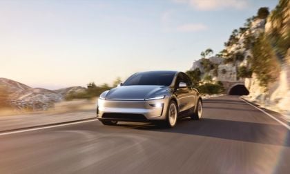 Silver 2026 Tesla Model Y Juniper driving on winding mountain road with rocky cliff and tunnel backdrop, motion blur showing dynamic movement