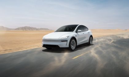 2025 Tesla Model Y, white, front three-quarter view, driving on a desert road with dust clouds.