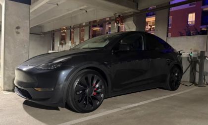 Midnight black 2025 Tesla Model Y charging in concrete parking garage, aggressive profile with black turbine wheels at night