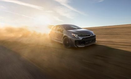 2023 Toyota Corolla in metallic gray, shown in three-quarter front view, driving on desert road at sunset with dramatic lighting and dust effects.