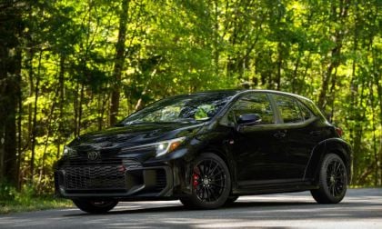 Black Toyota GR Corolla hatchback parked on forest road with sunlit green trees behind