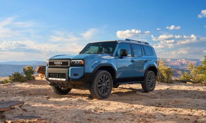 2025 Toyota Land Cruiser 250 Series in blue parked on rocky desert terrain, front three-quarter view highlighting off-road design.
