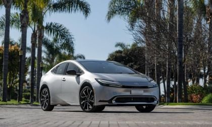Silver 2025 Toyota Prius shown from a front three-quarter angle on a palm-lined street, highlighting its low-slung stance, sharp LED headlights, and modern hybrid styling.