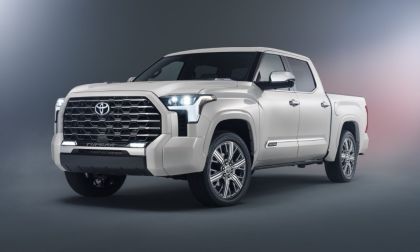 A white 2025 Toyota Tundra shown from a front three-quarter angle, featuring its bold new grille design, LED headlights, and chrome-finished alloy wheels against a dark studio background.