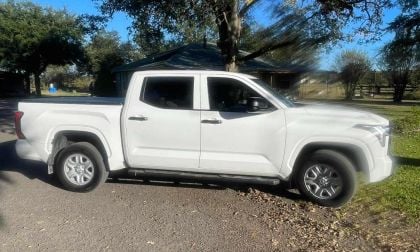 2025 Toyota Tundra crew cab pickup in white, photographed from passenger side, featuring chrome wheels and running boards, parked outside residential home.