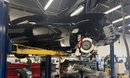 Chevrolet Corvette C8 on a lift with engine removed for repair inside an automotive service workshop.