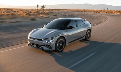 Gray Kia EV6 electric crossover driving on a desert highway at sunset, showcasing aerodynamic design and modern LED headlights.