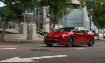 Red 2025 Toyota Prius driving through an urban street, showcasing sporty exterior styling and updated front fascia.