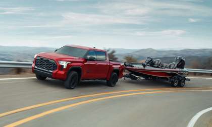 Red 2025 Toyota Tundra towing a fishing boat on a winding road, demonstrating the truck's towing capability.