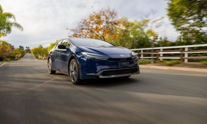 2025 Toyota Prius Limited in Reservoir Blue driving down a suburban street, front three-quarter view with motion blur and trees lining the road.