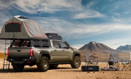 Tan 2025 Toyota Tacoma TrailHunter with rooftop tent parked in desert landscape with mountains, camping gear, and scenic sky